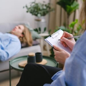 A therapy session in progress with a therapist taking notes as a patient reclines on a sofa.